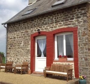 a brick building with benches and a white door at La Perruche Holiday Gite in Heussé