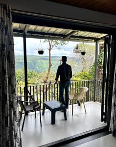 a man standing on a balcony looking out the window at Orchid View Villa Mahabaleshwar 2 Bhk Villa in Mahabaleshwar