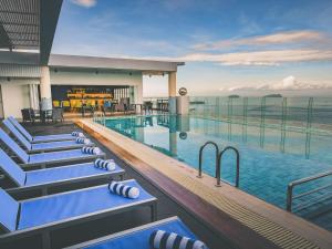 a hotel pool with lounge chairs and the ocean at Mercure Kota Kinabalu City Centre in Kota Kinabalu
