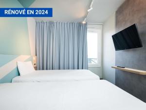 a hotel room with two beds and a television at Ibis Budget Lyon Caluire Cité Internationale in Caluire-et-Cuire