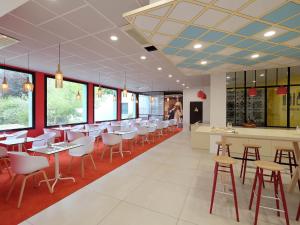 un restaurant avec des tables et des chaises blanches et des fenêtres dans l'établissement Hôtel ibis Styles Auxerre Nord, à Auxerre