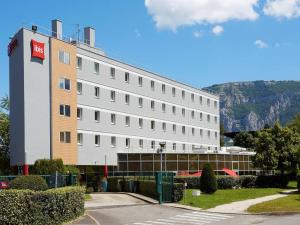a large white building with a mountain in the background at ibis Archamps Porte de Genève in Archamps