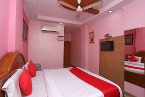 a bedroom with pink walls and a bed with red pillows at Hotel O Madhur Regency in Meerut
