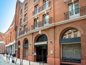 a red brick building with arches on a street at Mercure Toulouse Centre Wilson Capitole in Toulouse