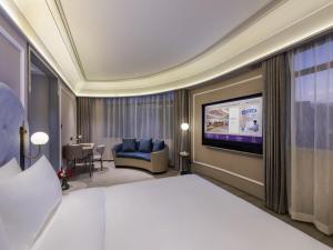 a hotel room with a bed and a flat screen tv at Mercure Qingdao Downtown in Qingdao
