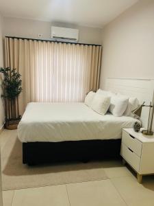 ein Schlafzimmer mit einem großen Bett mit weißen Laken und Kissen in der Unterkunft Willow Villa Apartments, at The Fig in Gaborone