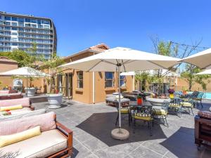 a patio with tables and chairs and an umbrella at Mercure Hotel Bedfordview in Johannesburg