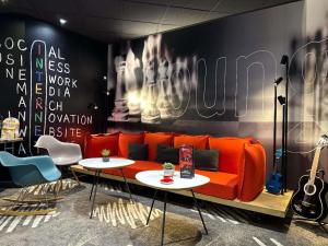 Una sala de estar con un sofá naranja y mesas. en ibis Alençon, en Alençon