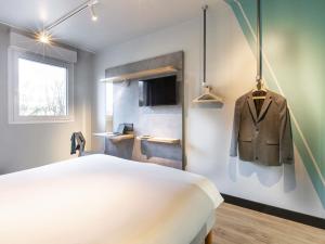 a bedroom with a bed and a suit hanging on a wall at ibis budget Saint Dié des Vosges in Saint Die