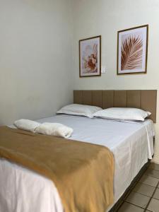 a bed with white sheets and two pictures on the wall at Hotel Pousada Calhau in São Luís