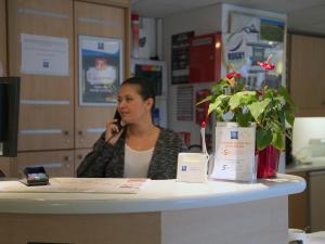 a woman sitting at a counter talking on a cell phone at ibis budget Niort - La Crèche in La Creche