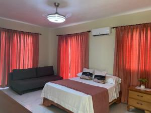 a bedroom with a bed and a couch and red curtains at Jeda Village in Higuey