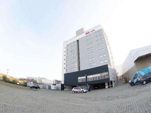 Un gran edificio con coches aparcados en un estacionamiento. en ibis Contagem Ceasa, en Contagem