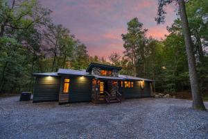 uma pequena cabana na floresta ao anoitecer em Wine Time 5 Bedroom Shuffleboard Hot Tub Fire Pit Play Set em Broken Bow