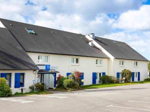 a large white house with blue doors and a street at Ibis budget Lorient Caudan in Caudan