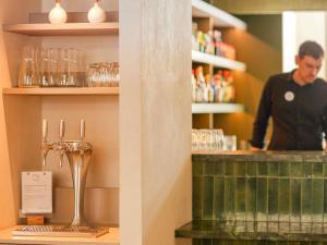 a man standing behind the counter of a bar with glasses at Mercure Colmar Centre Unterlinden in Colmar