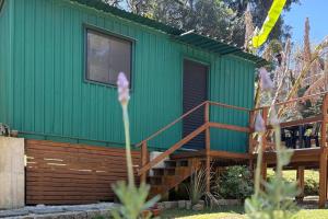 a green tiny house with a wooden staircase at Container Climatizado com deck em frente ao Parque do Passaúna by Tiny House Passaúna in Ferraria