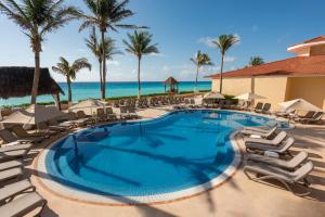 une piscine avec des chaises et des palmiers et l'océan dans l'établissement GR Solaris Cancun - All Inclusive, à Cancún