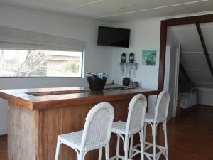 a kitchen with a wooden bar with three white stools at Ecos Oceano Ponta Malongane in Ponta Malongane