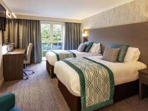 a hotel room with two beds and a desk at Mercure Milton Keynes Hotel in Milton Keynes