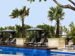 une piscine avec chaises, parasols et palmiers dans l'établissement Raffles Makati, à Manille