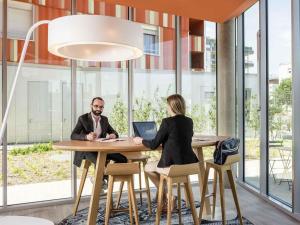 Un hombre y una mujer sentados en una mesa con una computadora portátil. en Aparthotel Adagio Access Paris Massy Gare, en Massy