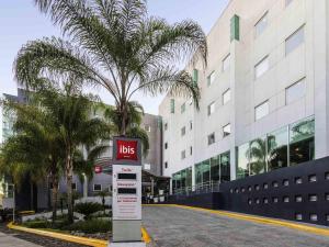 Un cartel de autobús frente a un edificio con una palmera. en Ibis Guadalajara Expo, en Guadalajara