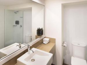 Un baño blanco con lavabo y espejo. en Mercure Sydney Parramatta, en Sídney