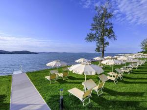 a row of chairs and umbrellas next to the water at Mövenpick Balaland Resort Lake Balaton in Szántód