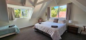 a bedroom with a large bed and two windows at Soggy Bottom Farm House, Sea views and peacocks in Pakawau