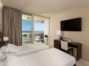 a hotel room with two beds and a desk and a window at Mercure Rimini Lungomare in Rimini