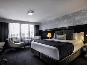 une chambre d'hôtel avec un grand lit et une chaise dans l'établissement Pullman Brisbane King George Square, à Brisbane