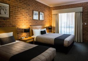 a hotel room with two beds and a brick wall at Akuna Motor Inn and Apartments in Dubbo