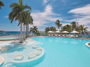 a large swimming pool with lounge chairs and palm trees at Mövenpick Hotel Mactan Island Cebu in Mactan