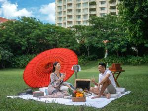 a man and woman sitting on a picnic blanket with an umbrella at Sofitel Phnom Penh Phokeethra in Phnom Penh