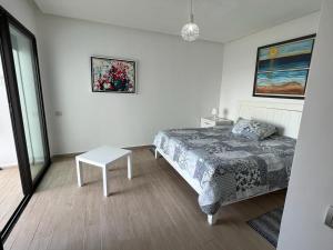 a white bedroom with a bed and a table at Luxurious Seaside Apartment in Sidi Bouqnadel