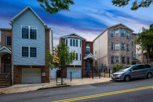 un'auto parcheggiata di fronte alle case in una strada di Newark Gem Ruby 3BR, 3BA - Sleeps 14 - Walk to Prudential Center and Newark Penn Station, Near EWR and American Dream Mall, includes Parking - WiFi - Laundry - Backyard - Gym a Newark