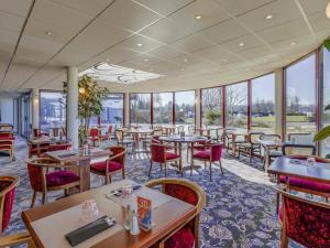 Un restaurante con mesas, sillas y ventanas. en Mercure Lyon Est Villefontaine, en Villefontaine