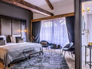 a bedroom with a bed and chairs and a large window at Mercure Figeac Viguier du Roy in Figeac