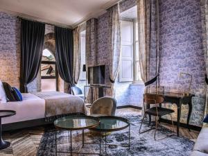 a bedroom with a bed and tables and a fireplace at Mercure Figeac Viguier du Roy in Figeac