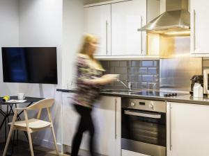 a woman walking in a kitchen with a stove at Aparthotel Adagio London Brentford in Brentford