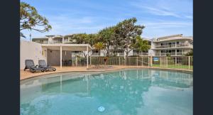 a swimming pool with two chairs in front of a building at Absolute Beachfront Apartment, Kawana Beach Escape in Buddina