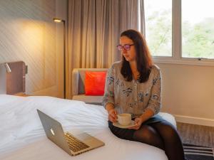 a woman sitting on a bed with a cup of coffee and a laptop at Novotel Sao Jose dos Campos in São José dos Campos +149 photos