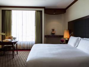 a hotel room with a bed and a desk and a window at Pullman Khon Kaen Raja Orchid in Khon Kaen