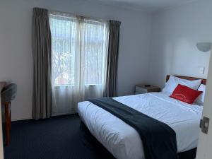 sypialnia z łóżkiem z czerwoną poduszką i oknem w obiekcie Ascot Motor Lodge w mieście Wellington