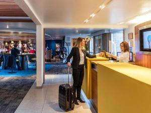 a woman standing at a counter with her luggage at Hôtel Novotel Valenciennes in Valenciennes