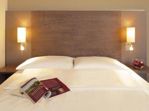 a book on a white bed with two lamps at Mercure Hotel Frankfurt Eschborn Ost in Eschborn