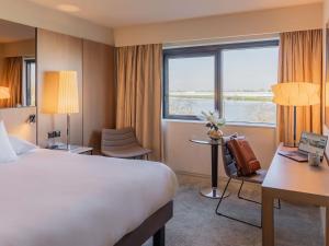 a hotel room with a bed and a desk and a window at Pullman Bordeaux Lac in Bordeaux