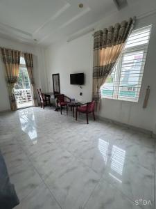 a living room with a table and chairs and windows at Nhà Nghỉ Hoàng Gia Phát in Buôn Kô Sir
