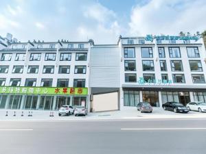 Un gran edificio blanco con coches aparcados delante. en Magnotel Hotel Huangshan Scenic Area Transfer Center, en Huangshan Scenic Area